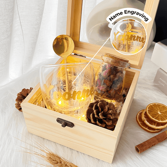 name engraved glass next to a rose petal filled jar with a gold spoon in a wooden gift box
