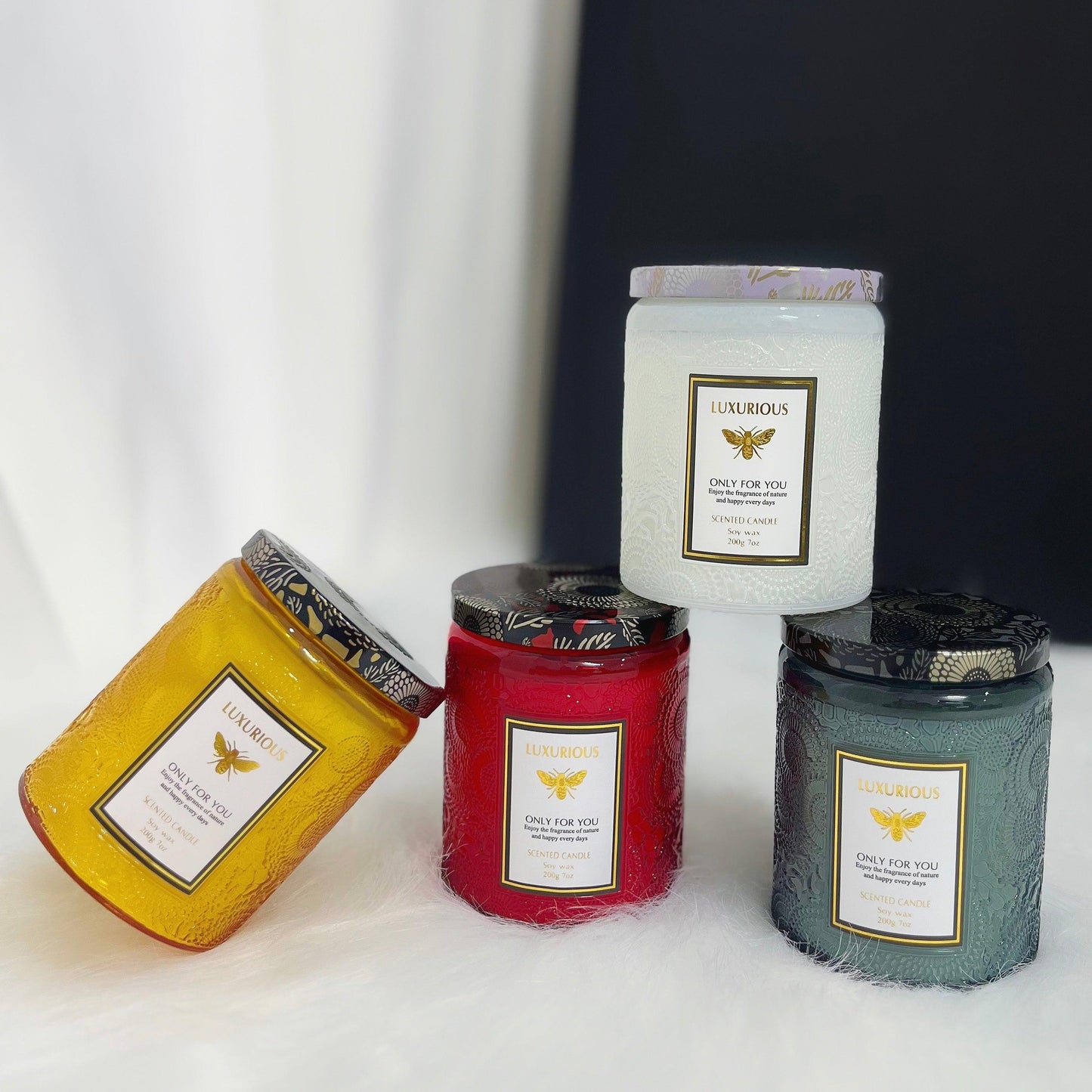 4 luxurious scented candles over a white clothed table stacked over each other as a display