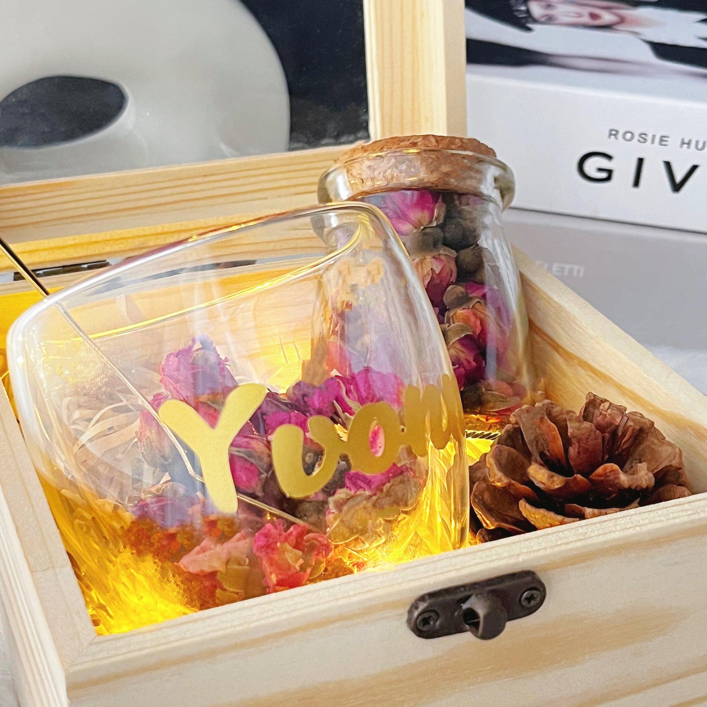 close up shot of the name engraved glass cup with rose petal tea in it with glowing fairy lights from the gift box