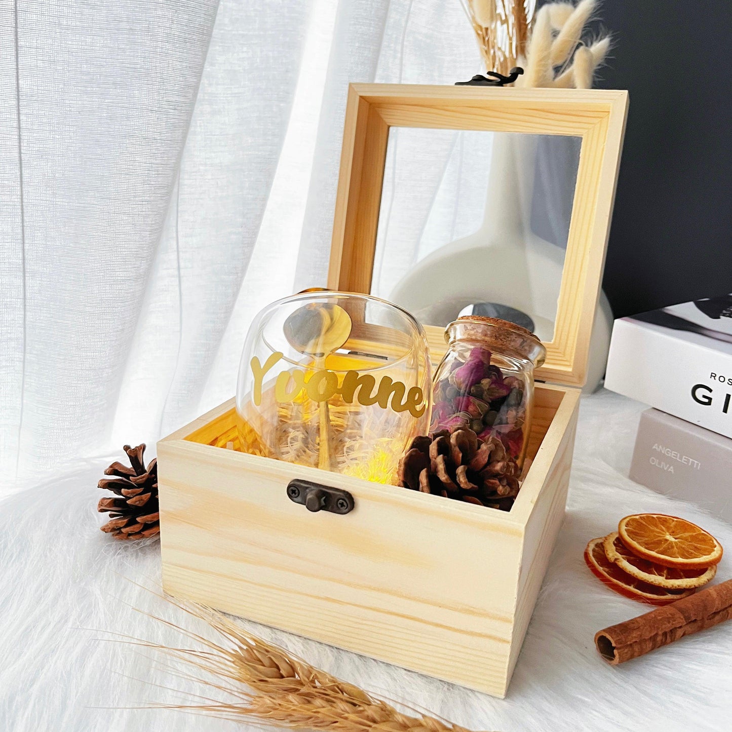 a wider angle shot of the petal and cup gift box with pinecones and orange slices as props next to it over a white and black background